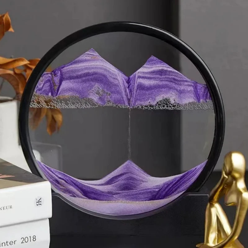 Circular Soulful Trading 3D Moving Sandscape frame displaying a purple and silver layered landscape, positioned on a desk beside books and a decorative figurine.