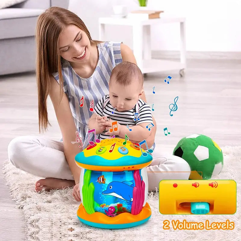 A woman smiles at a baby playing with a colorful Soulful Trading Enchanting Baby Musical Ferris Wheel on a carpeted floor; text indicates &quot;2 volume levels.