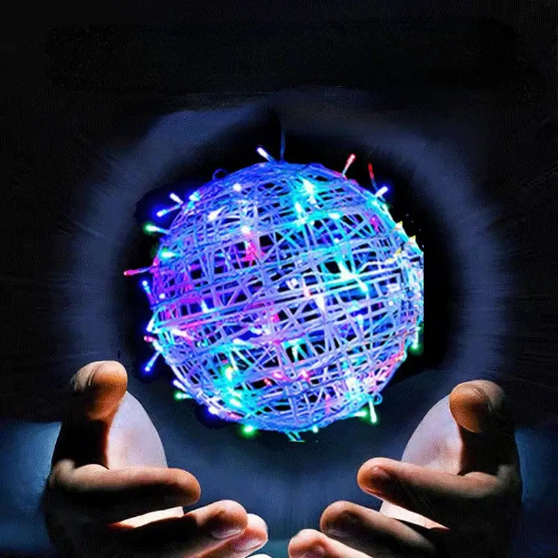 Glowing multicolored Soulful Trading Fly Nova Pro Drone Ball with lights, held delicately between two hands against a dark background.
