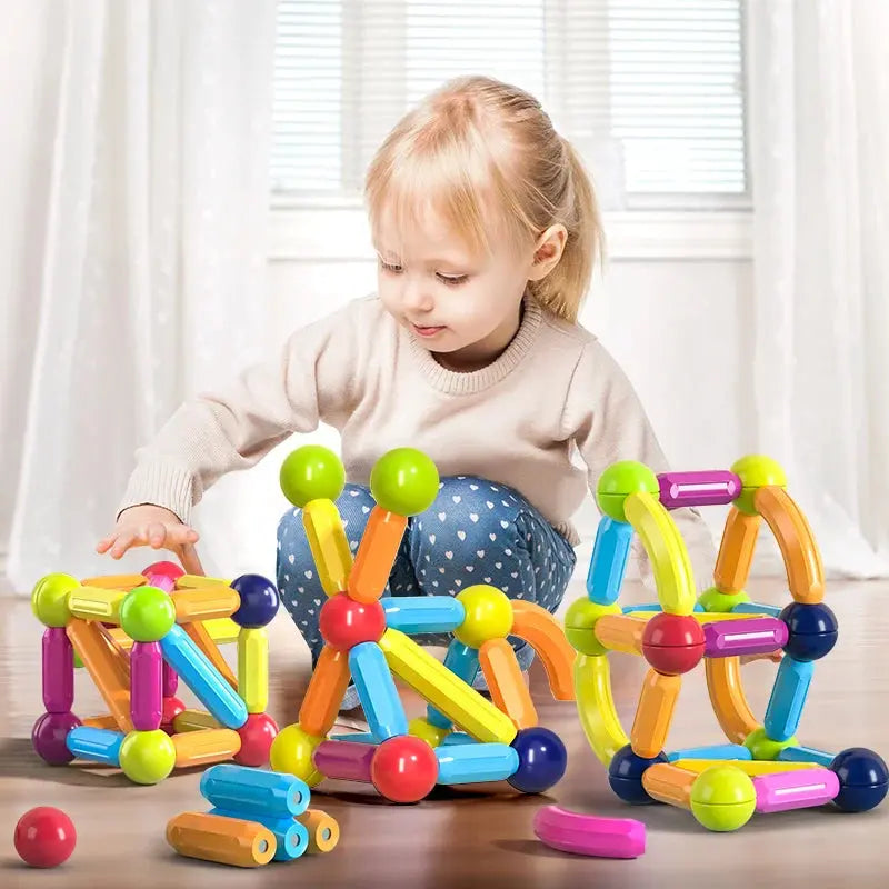 A young girl plays with colorful Soulful Trading Magnetic Sticks Building Blocks and balls on a floor indoors, promoting STEM educational development.