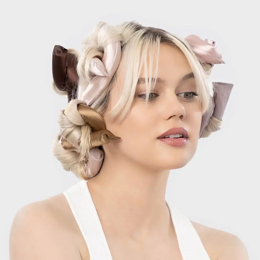 A woman with an avant-garde hairstyle featuring large satin bows and soft, sculptural Lazy Heatless Curls created using a Soulful Trading curling rod, set against a plain white background.