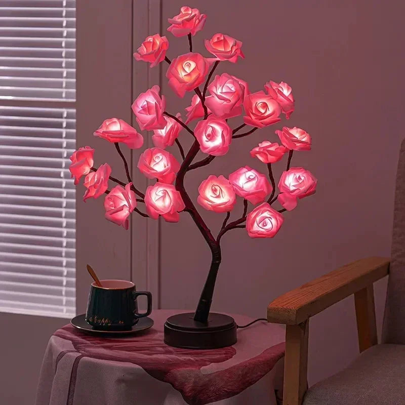 A decorative Soulful Trading Forever Rose Tree Lamp with pink illuminated flowers on a table beside a black coffee mug, set against a mauve curtain backdrop.