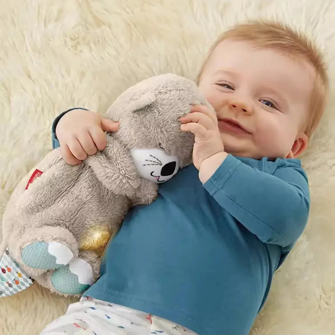 A smiling baby lying on a soft blanket, hugging a plush Soulful Trading Sleep Buddy bunny toy.