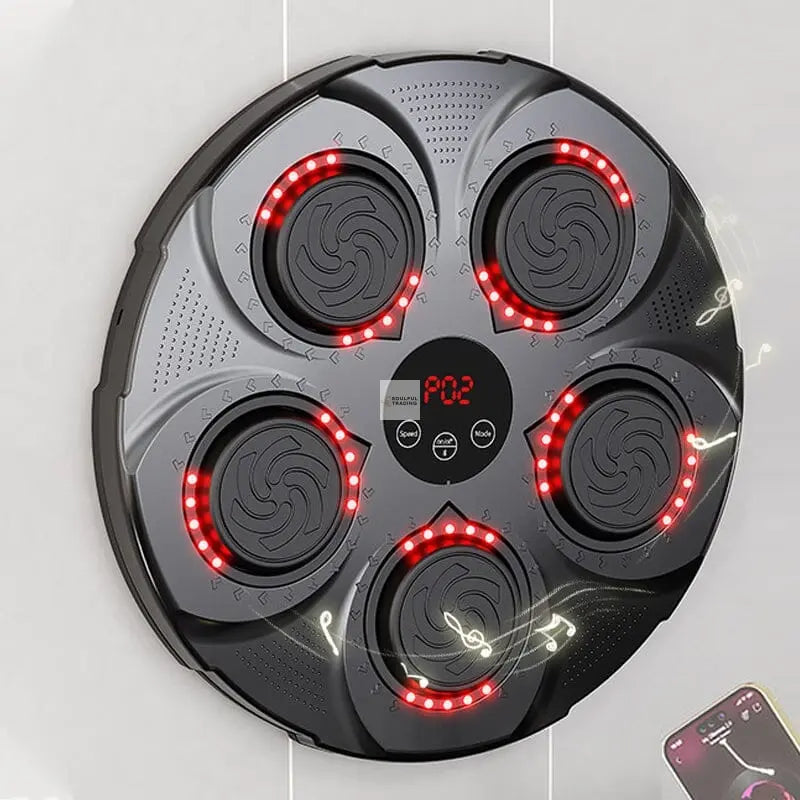 Top view of a modern, circular black electric stove with six red glowing induction hobs and a digital display, with a Bluetooth-connected smartphone showing the Soulful Trading Music Boxing Machine control app nearby.