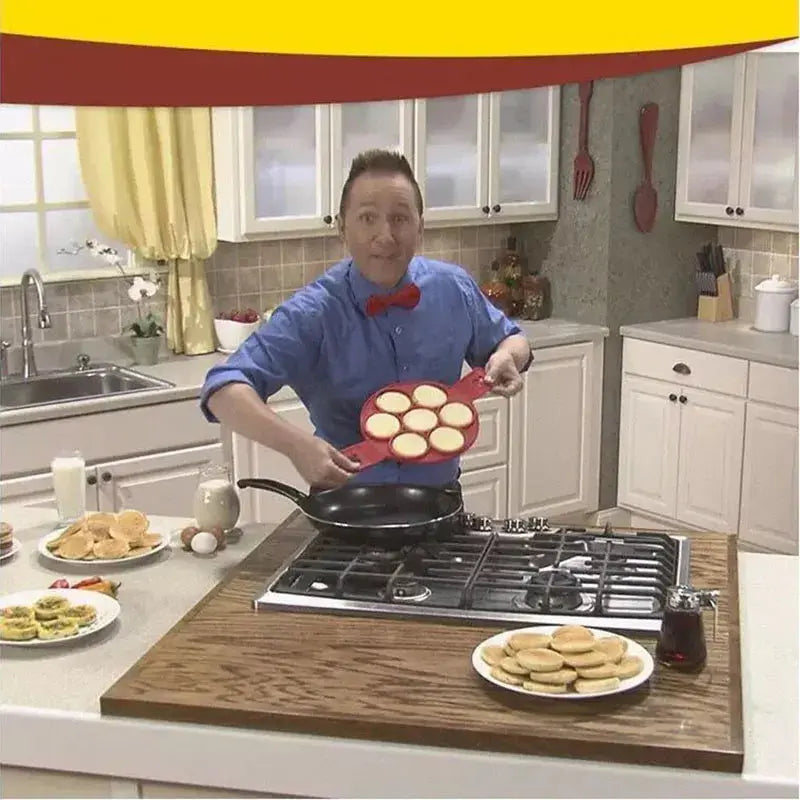 A person in a blue shirt and red bow tie cooking pancakes in a kitchen, holding a skillet with several pancakes over a stove, using a Soulful Trading Flip &