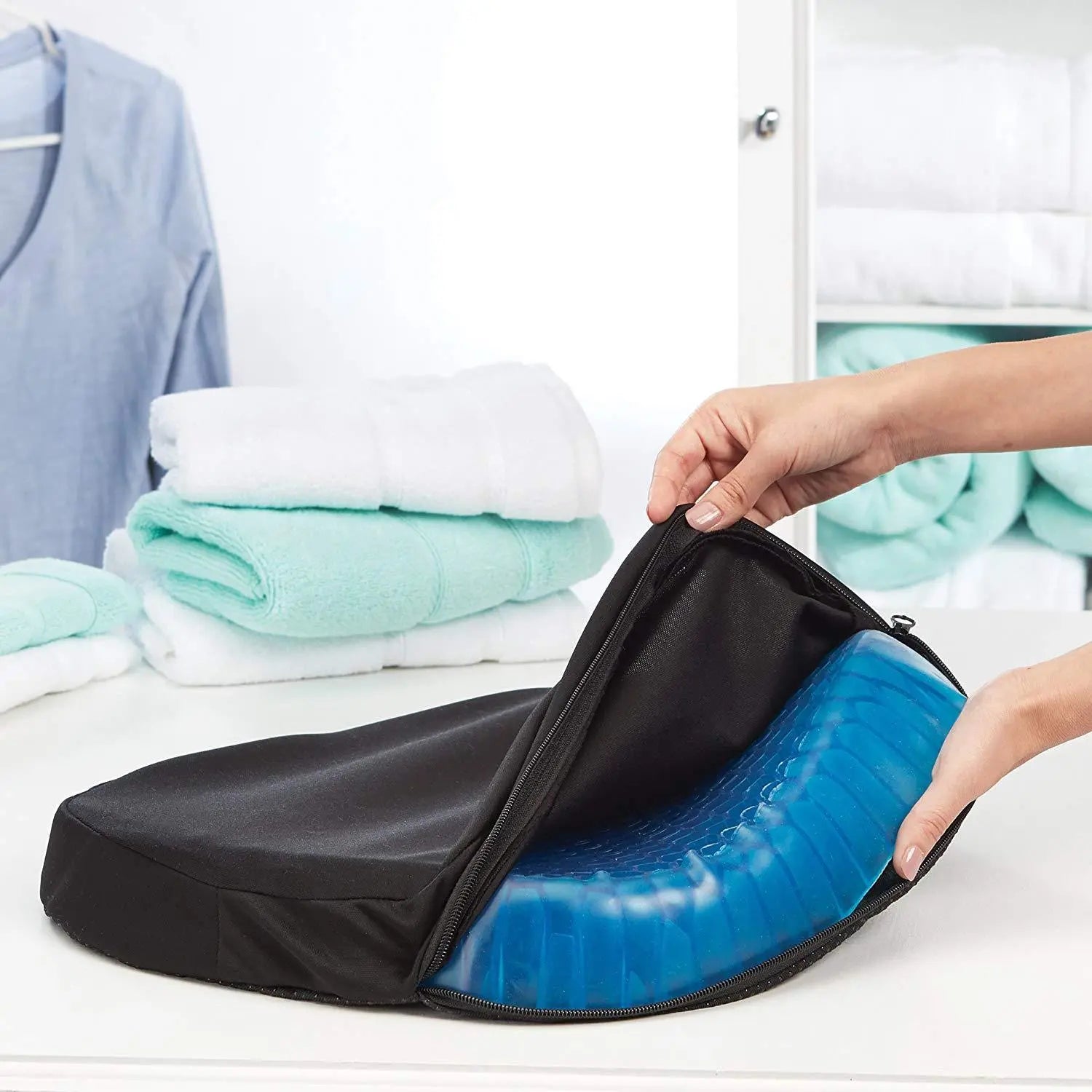 A person unzipping a black carrying case to reveal a blue Home Essentials-5 Elastic Silicone Gel Cushion inside, placed on a white countertop with folded towels in the background.