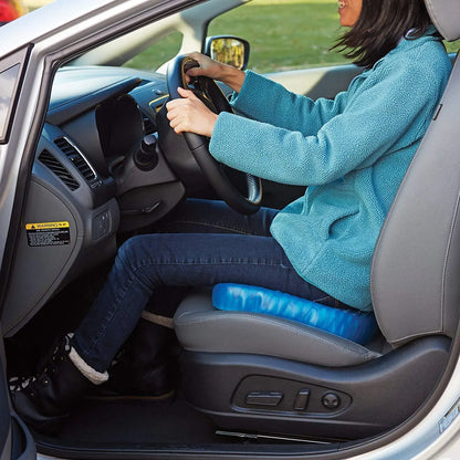 A woman driving a car, using a Home Essentials-5 Elastic Silicone Gel Cushion, wearing a teal jacket and black pants.